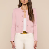 Woman wearing a pink jacket over a white top and beige pants on a beige background