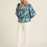Woman wearing a blue floral blouse and white pants on a beige background