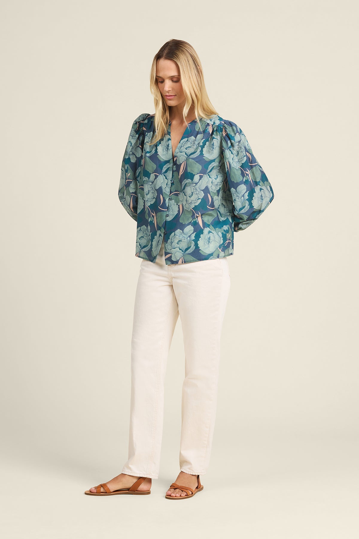 Woman wearing a blue floral blouse and white pants on a beige background