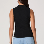 Woman wearing a black sleeveless knitted top and light blue jeans on a plain background