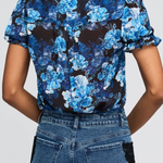 A woman shown from the back wearing a short-sleeve button-up blouse with a blue and black floral print, paired with blue jeans.