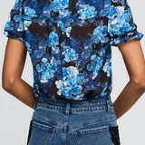 A woman shown from the back wearing a short-sleeve button-up blouse with a blue and black floral print, paired with blue jeans.