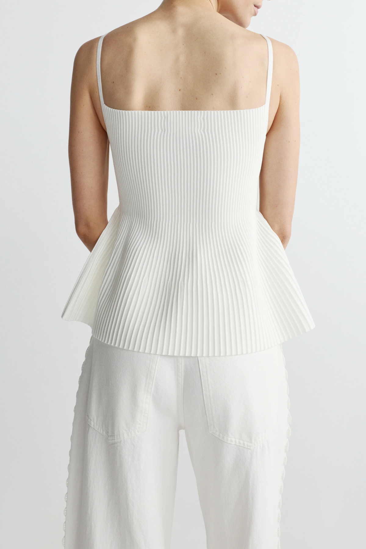 back of woman in ribbed white peplum tank on white background 