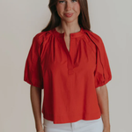 Woman wearing a red blouse with puff sleeves against a plain background