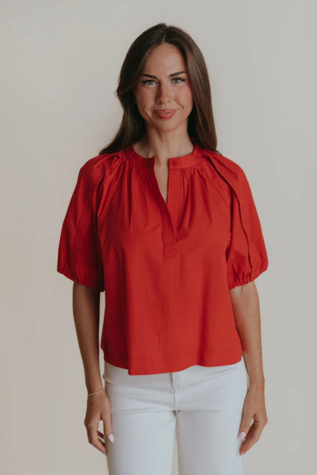 Woman wearing a red blouse with puff sleeves against a plain background