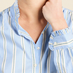 Close-up of a model wearing a light blue button-up shirt with vertical white stripes and ruffled trim on the collar and cuffs.