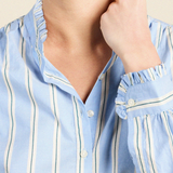 Close-up of a model wearing a light blue button-up shirt with vertical white stripes and ruffled trim on the collar and cuffs.