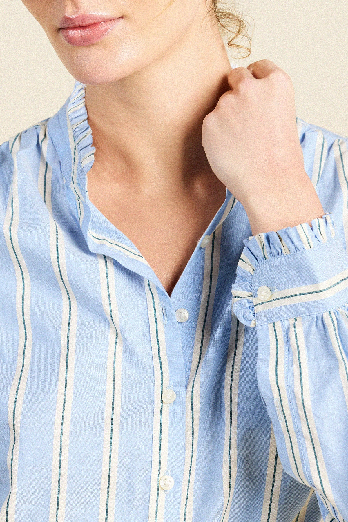 Close-up of a model wearing a light blue button-up shirt with vertical white stripes and ruffled trim on the collar and cuffs.