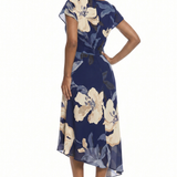 A woman modeling a navy blue midi dress with a large cream and gray floral print, shown from a side-back angle against a plain white background.