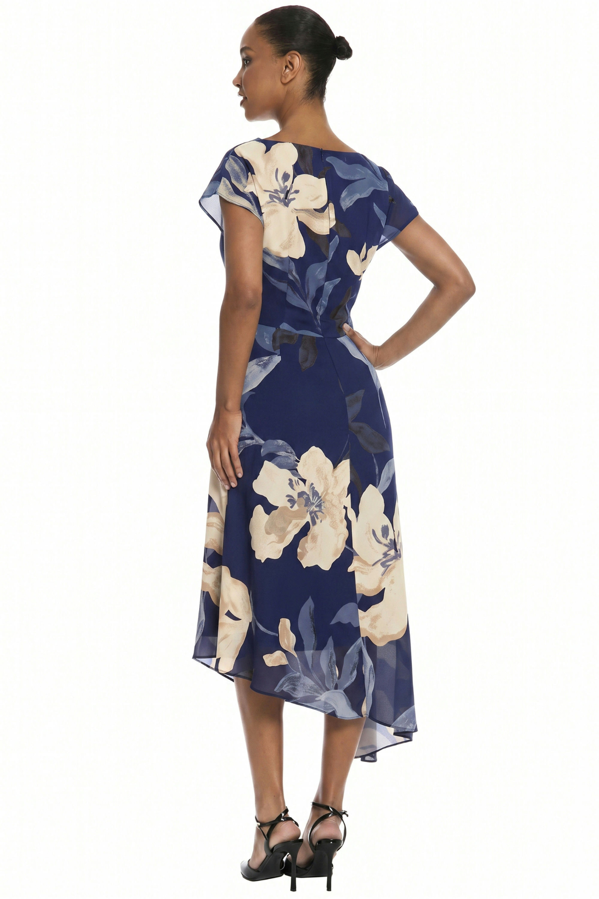 A woman modeling a navy blue midi dress with a large cream and gray floral print, shown from a side-back angle against a plain white background.