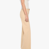 A woman shown from the side wearing a cream short-sleeve top, beige wide-leg trousers, and black high heels against a plain light gray studio background.