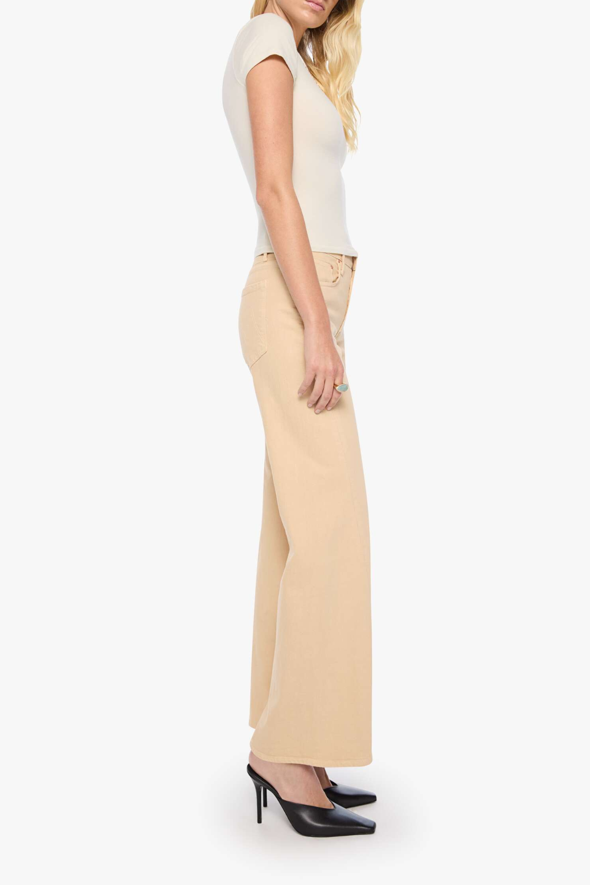 A woman shown from the side wearing a cream short-sleeve top, beige wide-leg trousers, and black high heels against a plain light gray studio background.