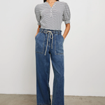 Woman wearing a striped shirt and blue jeans standing against a plain background