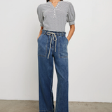 Woman wearing a striped shirt and blue jeans standing against a plain background