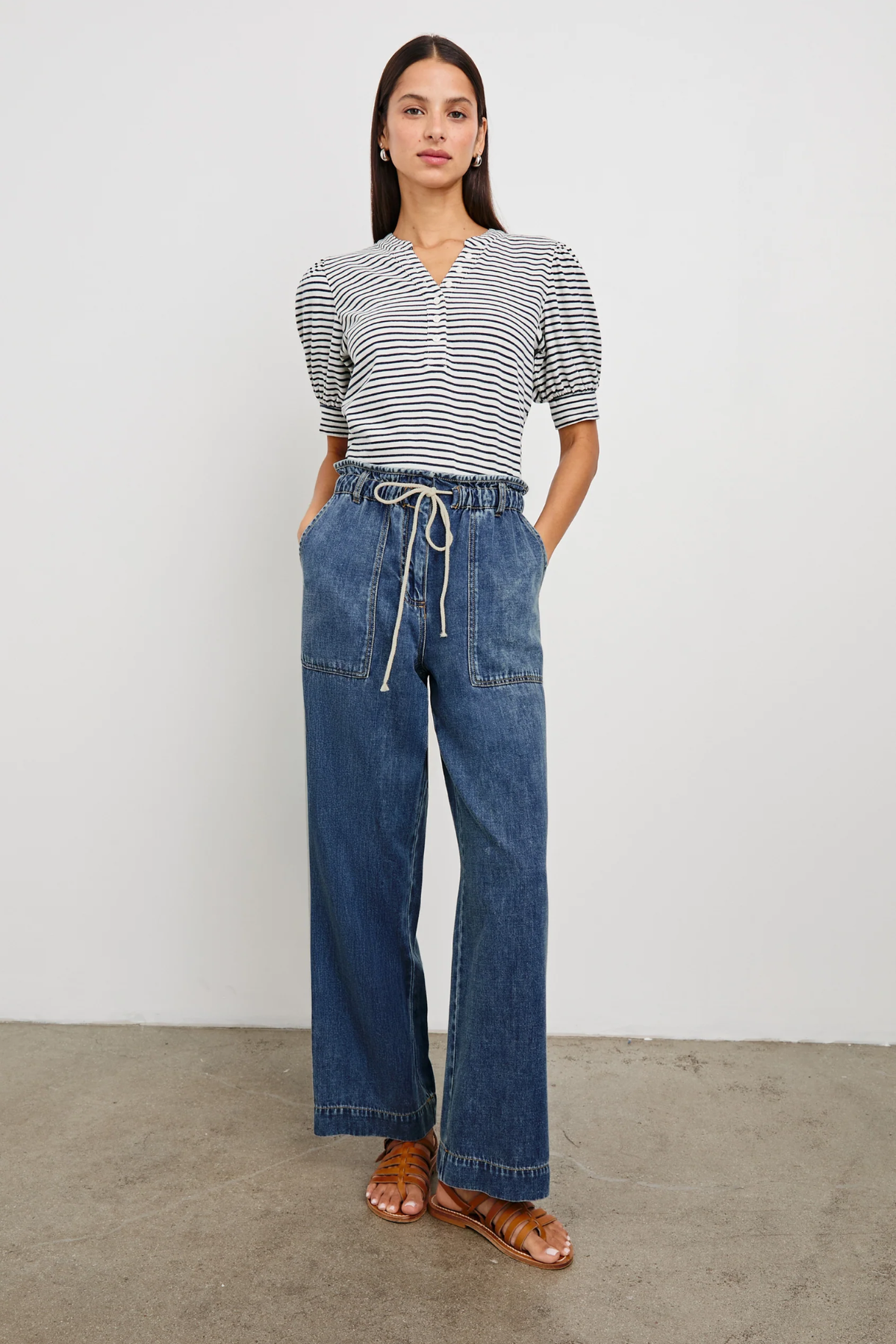 Woman wearing a striped shirt and blue jeans standing against a plain background