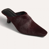 A single dark burgundy faux-hair mule heel shoe with a pointed toe, shown from a three-quarters angle on a light off-white background.