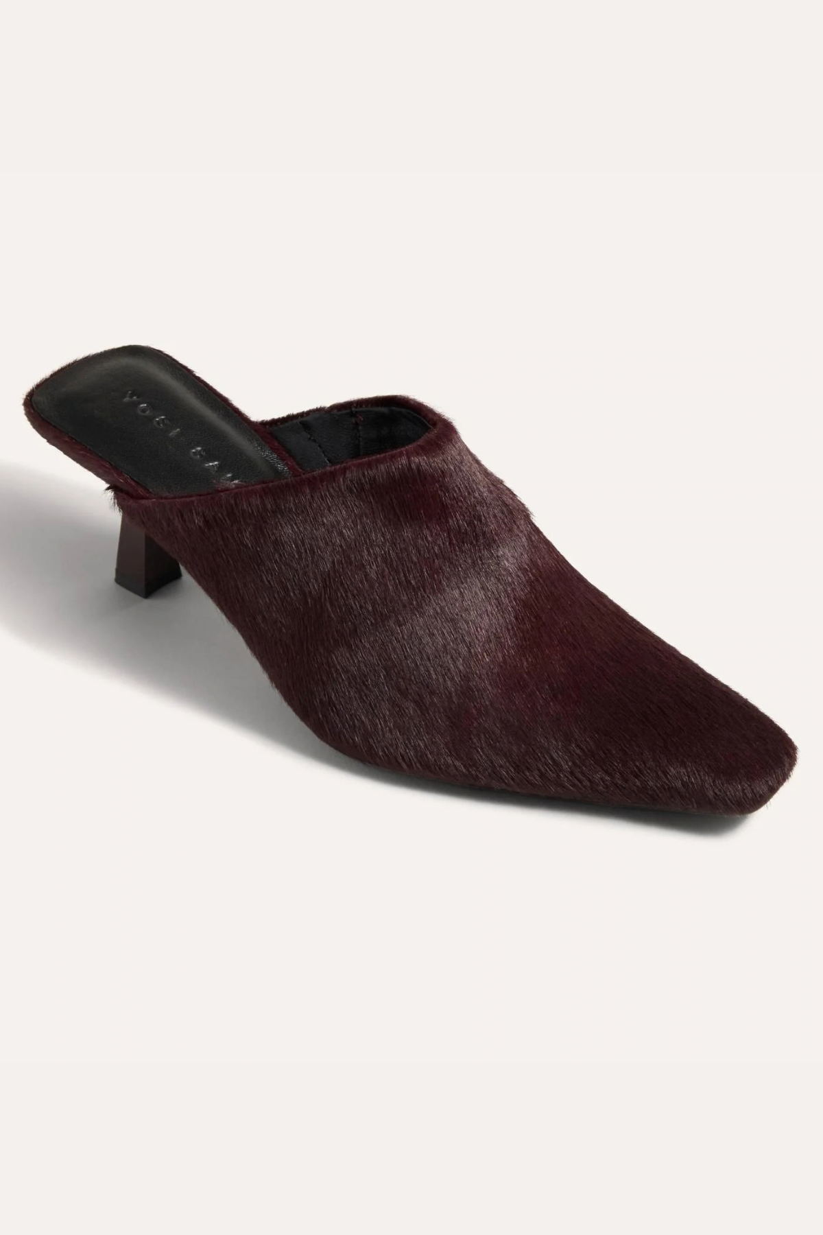 A single dark burgundy faux-hair mule heel shoe with a pointed toe, shown from a three-quarters angle on a light off-white background.