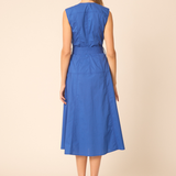 back of woman in blue belted dress on tan background 