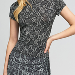 A woman wearing a fitted short-sleeve dress with a gray and black snakeskin pattern, shown from the shoulders to mid-thigh against a light gray studio background.