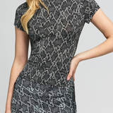 A woman wearing a fitted short-sleeve dress with a gray and black snakeskin pattern, shown from the shoulders to mid-thigh against a light gray studio background.
