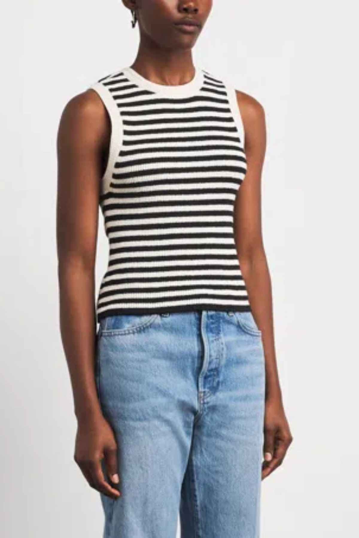 A model wearing a black and white horizontally striped sleeveless knit top paired with light blue jeans, photographed against a clean white studio background.