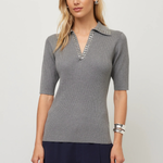 A woman modeling a gray ribbed knit polo shirt with a decorative silver beaded collar, paired with navy blue pants, against a light gray studio background.