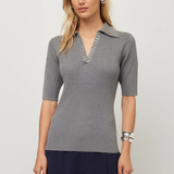 A woman modeling a gray ribbed knit polo shirt with a decorative silver beaded collar, paired with navy blue pants, against a light gray studio background.