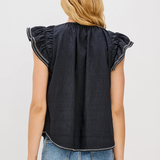 Person wearing a black sleeveless top with ruffled shoulders and blue jeans on a light gray background