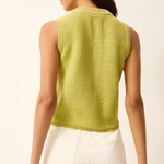 Woman wearing a green sleeveless knitted top and white shorts on a beige background