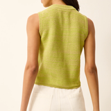 Woman wearing a green sleeveless knitted top and white shorts on a beige background