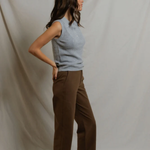 Woman wearing a light blue sleeveless top and brown pants against a plain background