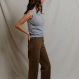 Woman wearing a light blue sleeveless top and brown pants against a plain background