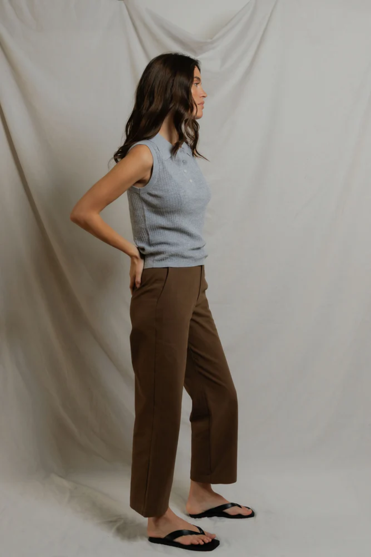 Woman wearing a light blue sleeveless top and brown pants against a plain background
