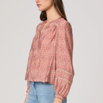 Woman wearing a pink patterned blouse and blue jeans on a plain background