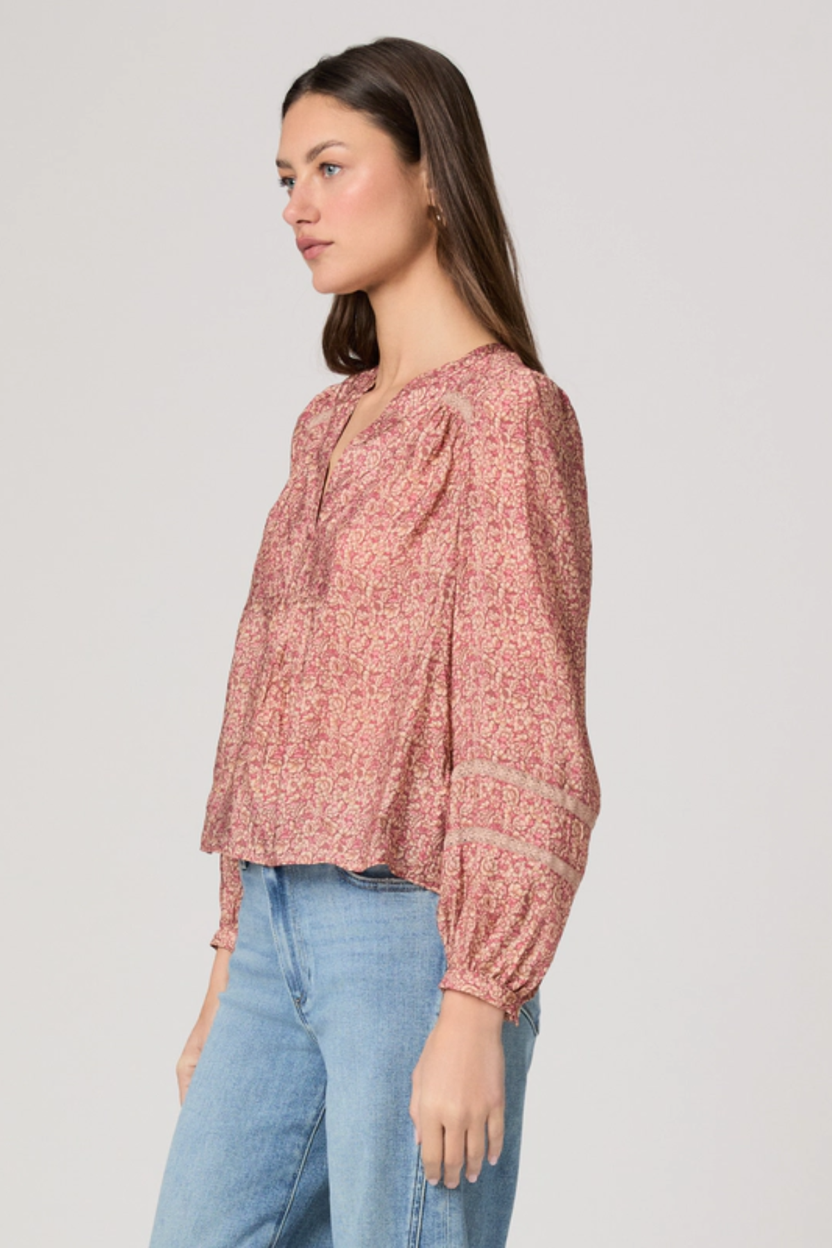 Woman wearing a pink patterned blouse and blue jeans on a plain background