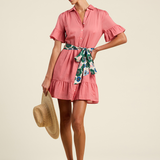 Woman wearing a pink dress with a floral scarf, standing against a beige background