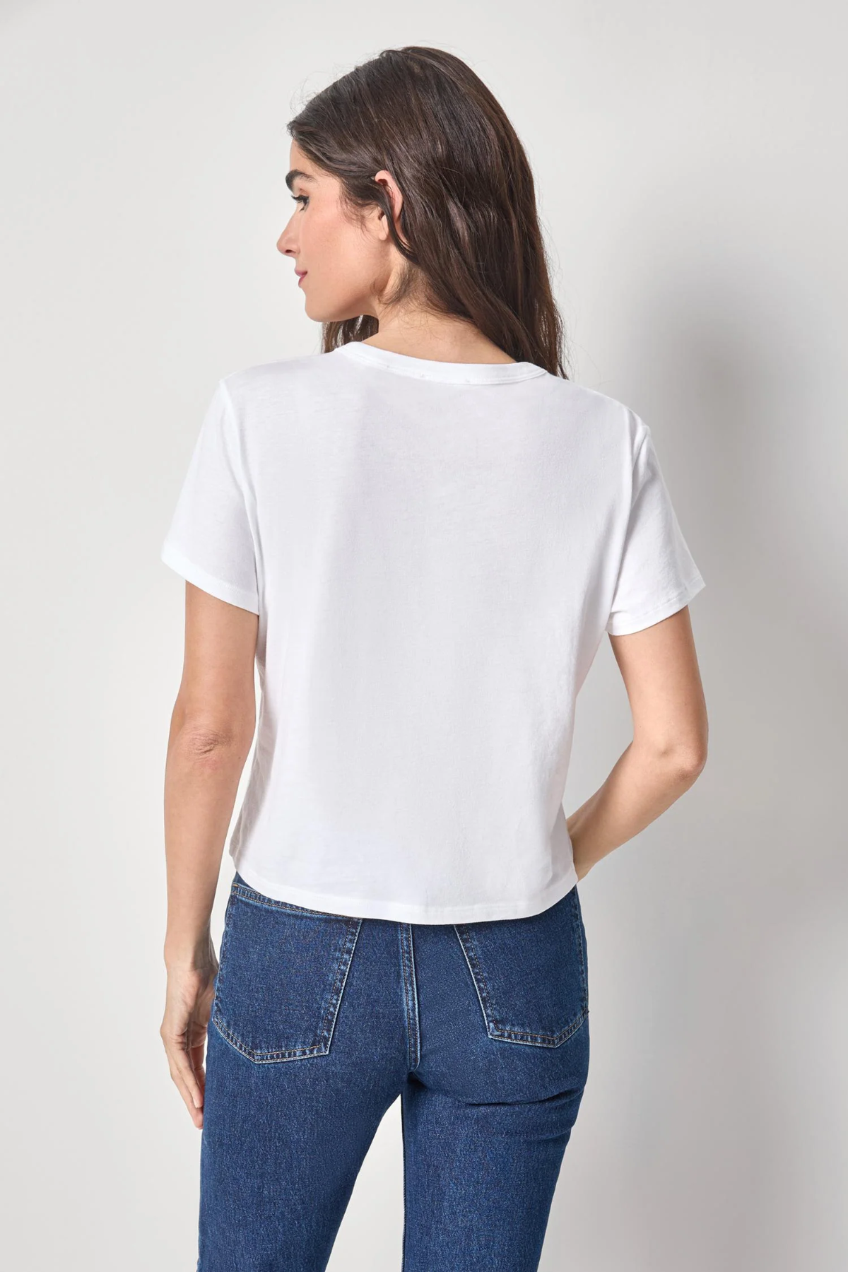 Woman wearing a white t-shirt and blue jeans against a plain background