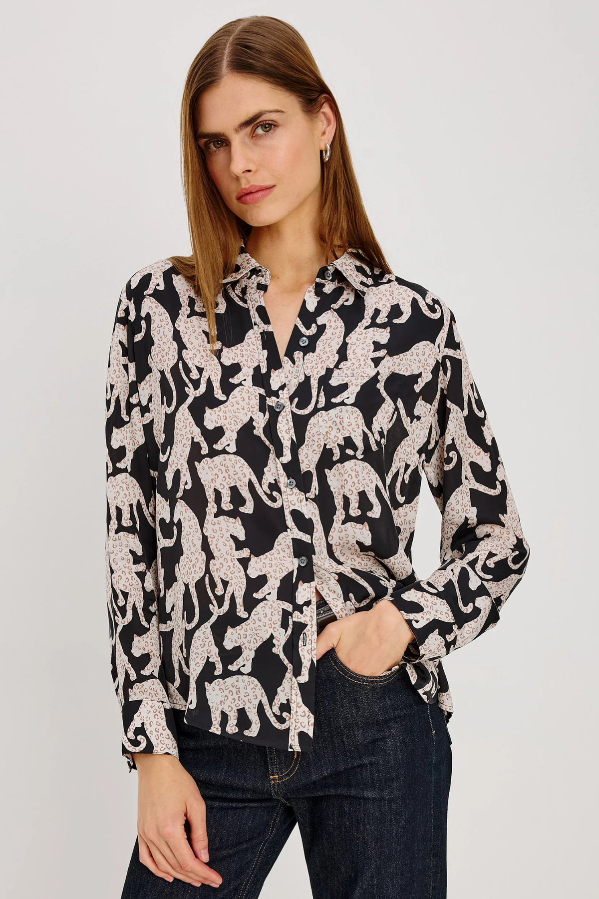 A woman modeling a black long-sleeve button-up shirt with a white leopard print pattern, paired with dark blue jeans, against a plain light gray background.