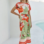 Woman wearing a colorful floral dress standing by a poolside.