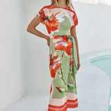 Woman wearing a colorful floral dress standing by a poolside.