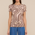 Model wearing swirl pattern tee with loose fitting jeans on beige background.