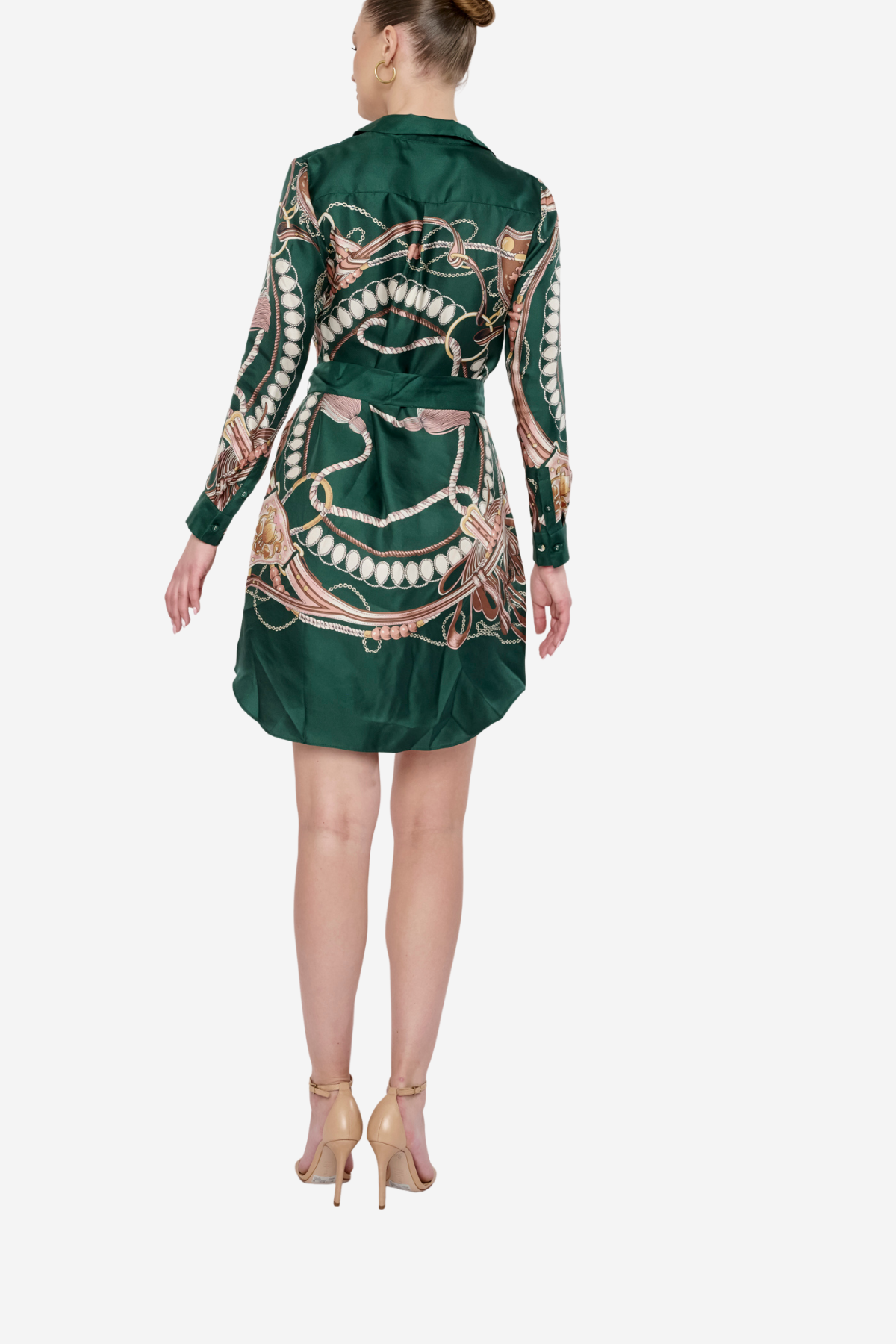 A woman viewed from the back wearing a dark green satin shirt dress with a large gold and white chain print, paired with beige high-heeled sandals, against a light gray background.