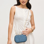 Woman in a white dress holding a blue clutch against a plain background