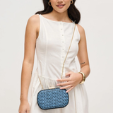 Woman in a white dress holding a blue clutch against a plain background