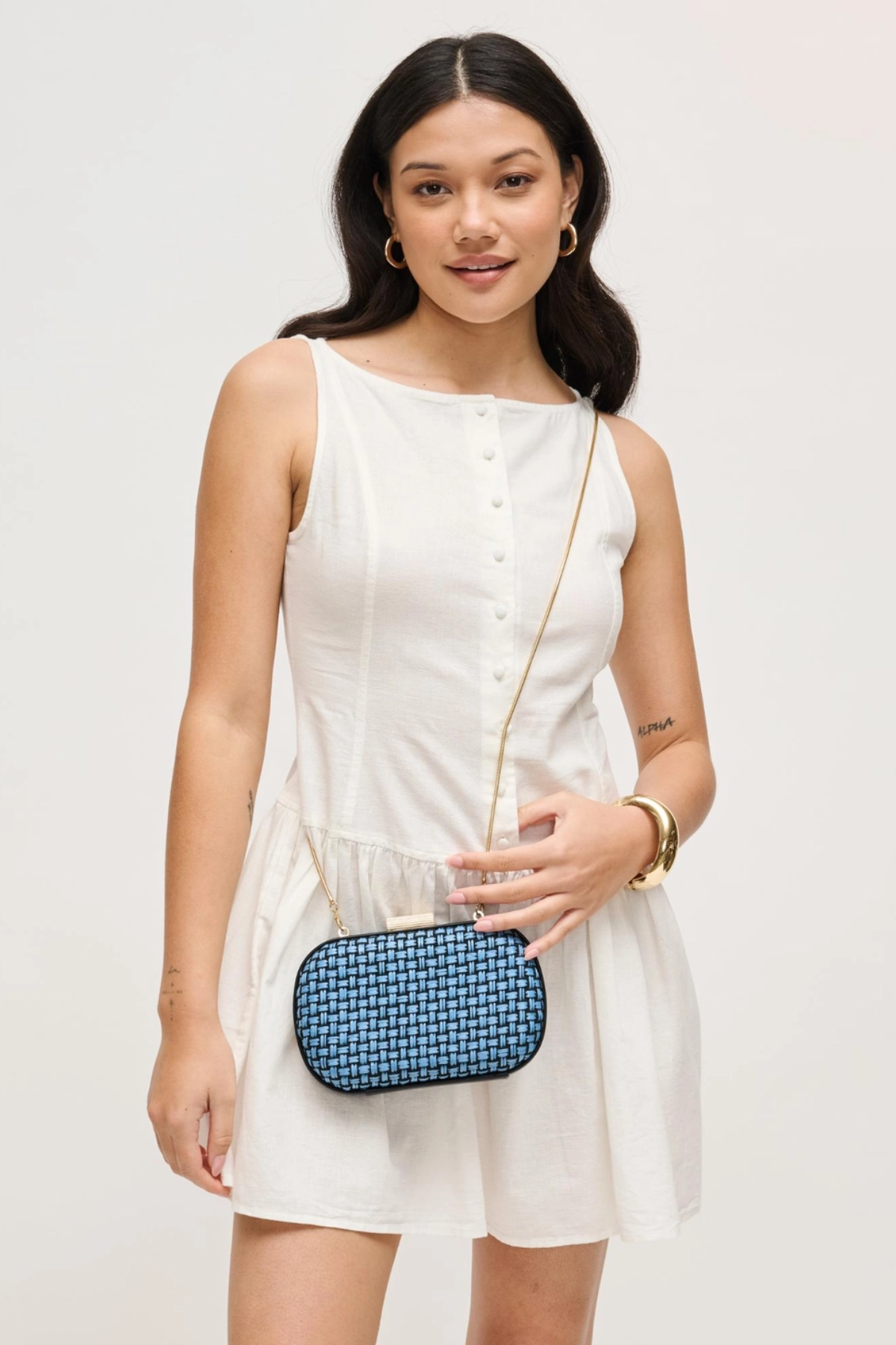 Woman in a white dress holding a blue clutch against a plain background