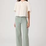 Woman wearing a white blouse and light green pants on a white background