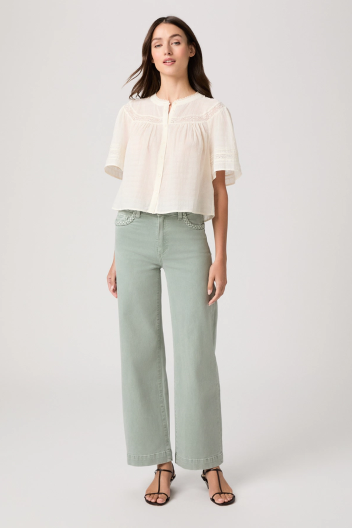 Woman wearing a white blouse and light green pants on a white background