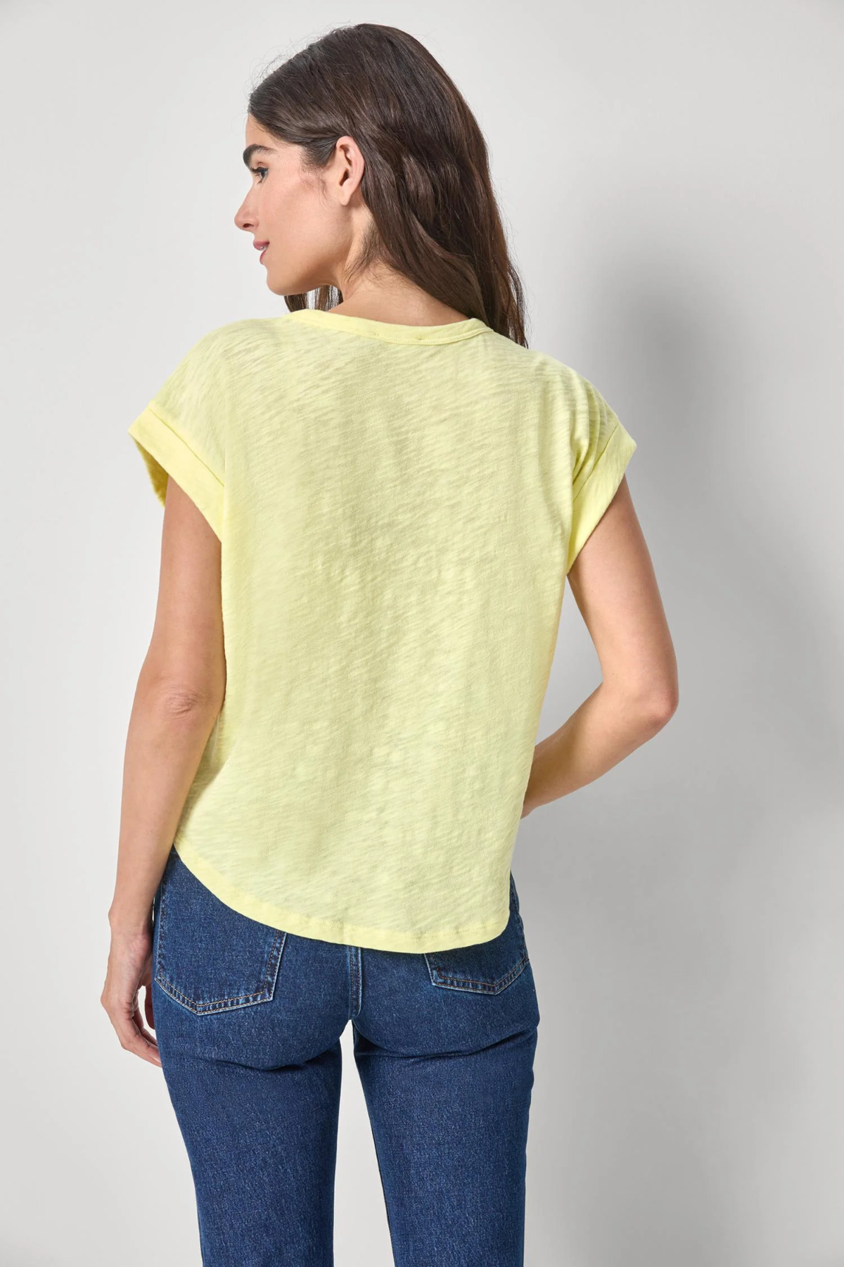 Woman wearing a light yellow top and blue jeans on a plain background