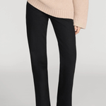A model wearing black wide-leg trousers and a beige ribbed knit sweater, shown from the chest down against a light gray studio background.