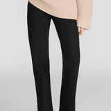 A model wearing black wide-leg trousers and a beige ribbed knit sweater, shown from the chest down against a light gray studio background.